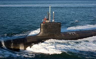 Image of part of the submarine, which is over the surface of the water. The water is deep blue and it is a sunny day out. 
