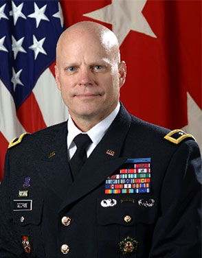 Picture of Major General John A. George. MG George is seated in front of the US flag and wears an army uniform with badges and insignia. He is smiling with a closed mouth at the viewer. 