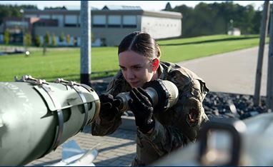 Female ammo tech inserting a DSU-33 Proximity Sensor into the back of a munition. A grey government building is behind her. 