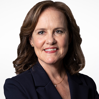 Image of the Honorable Michèle Flournoy. Flournoy is standing in front of a white background. She has light brown hair and is wearing a black blazer. She smiles with her teeth showing.